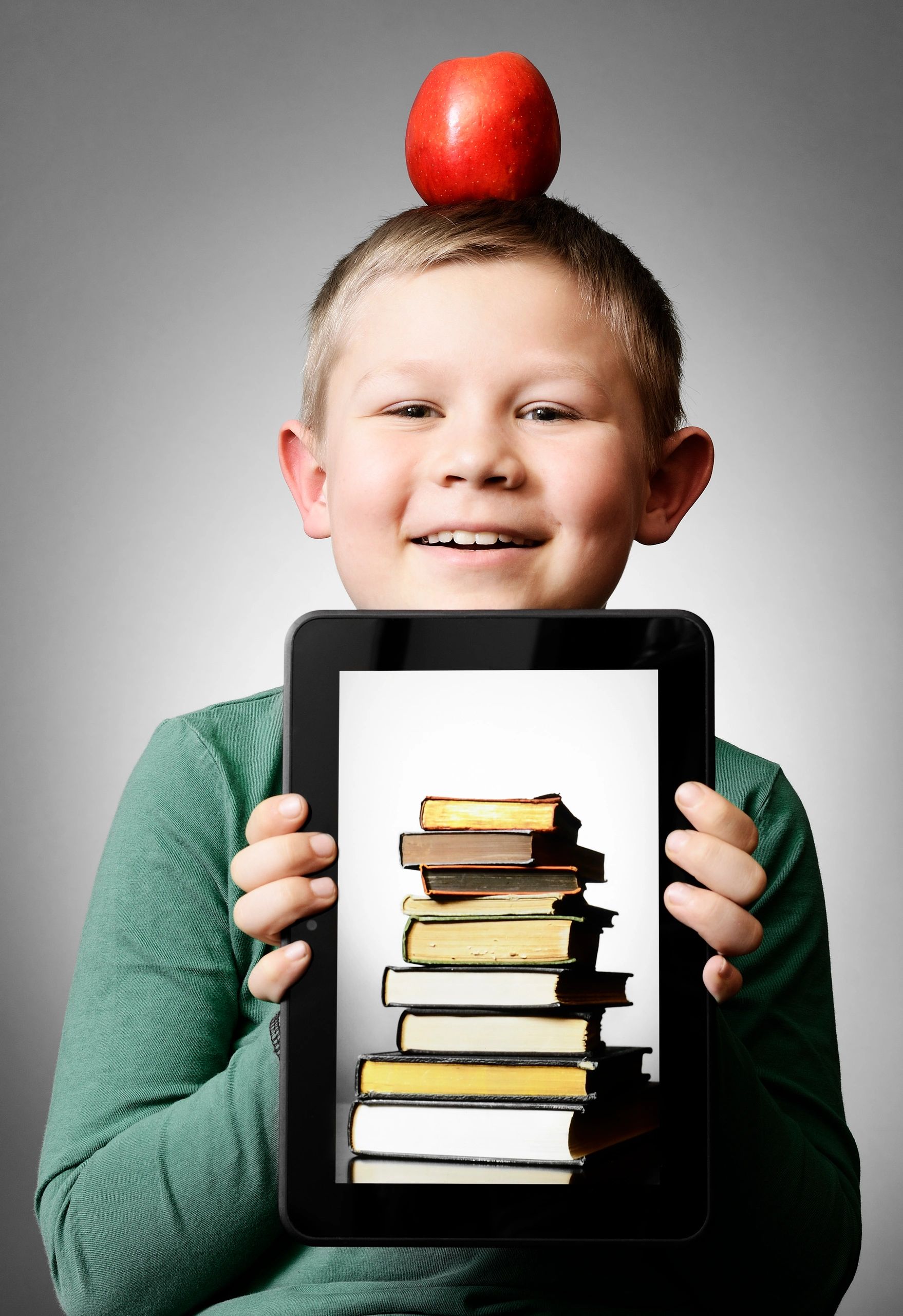 Boy with apple holding a tablet displaying books.